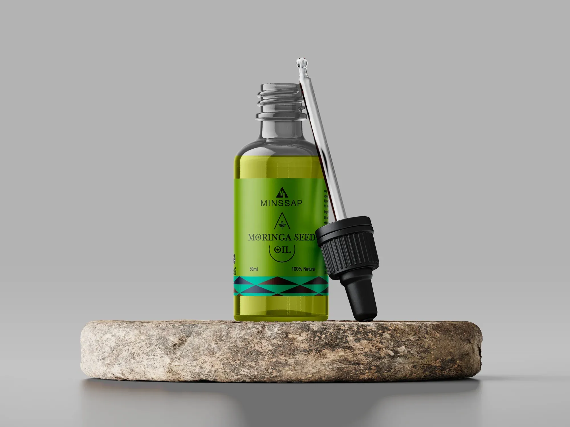 A moringa seed oil dropper bottle standing on a rough stone slab, its pipette lifted beside it.