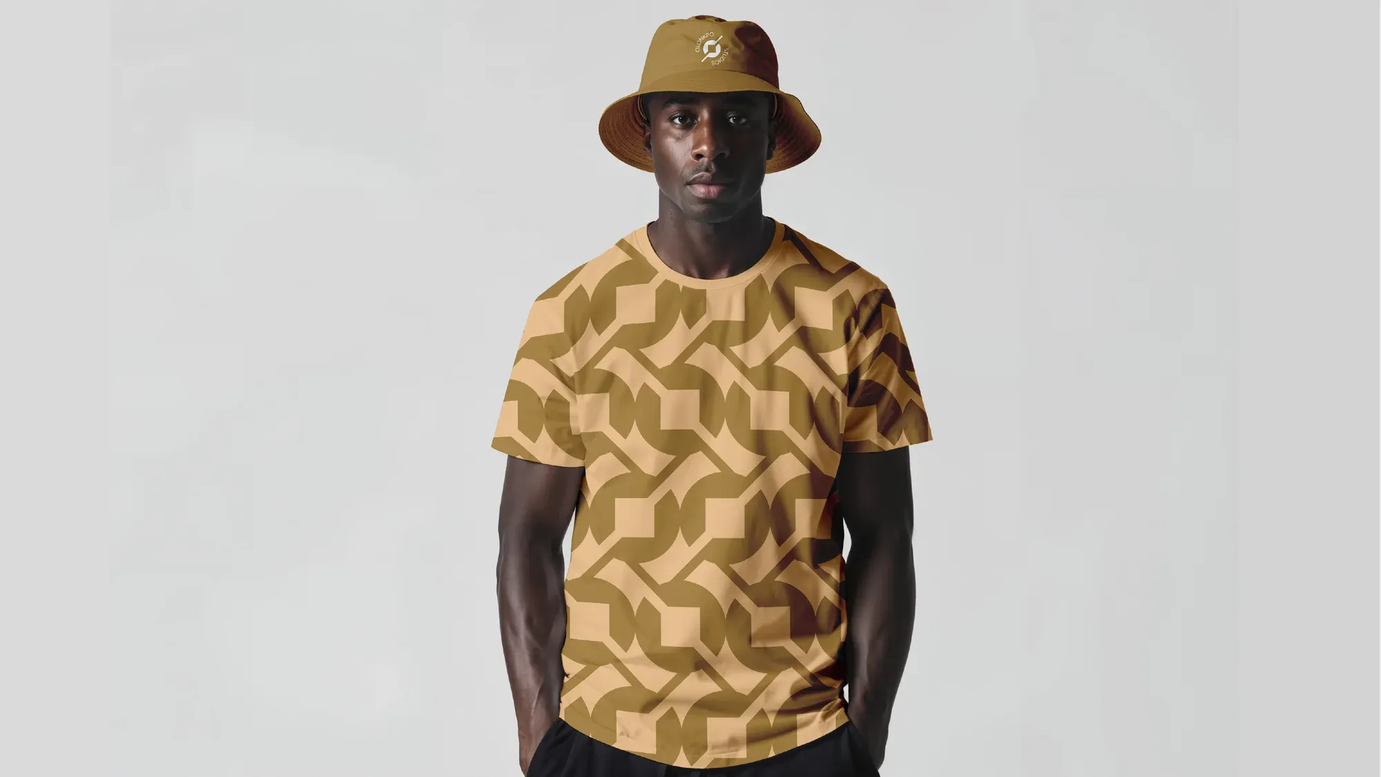 A model in a bucket hat and tee cut from the same gold interlocking pattern.