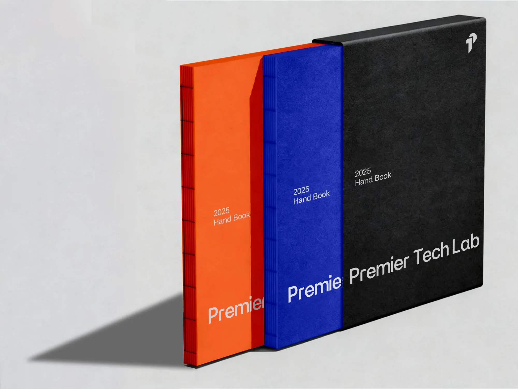 Three slipcased hand books standing side by side in orange, blue and black.