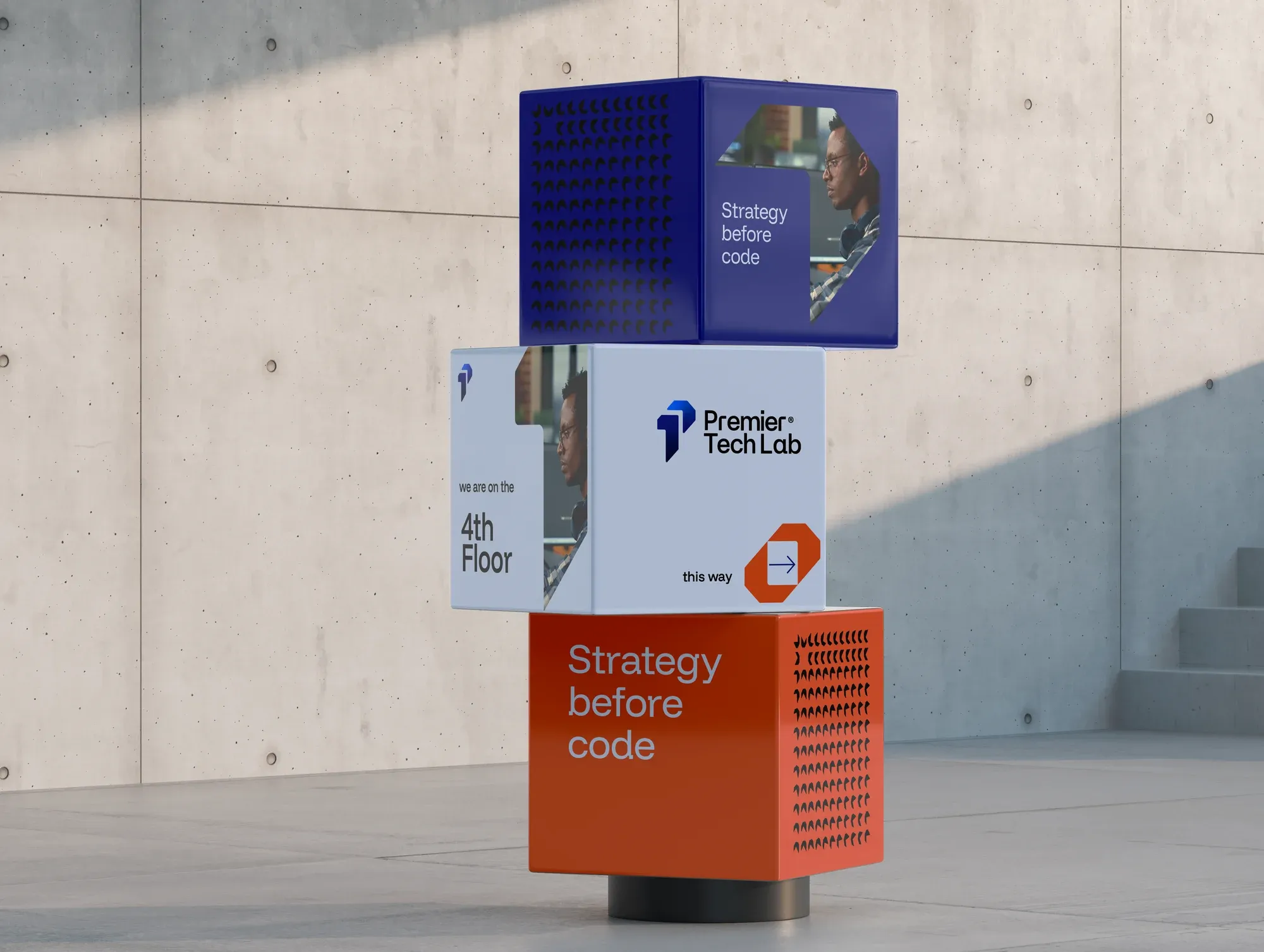 Stacked cube signage against concrete, reading strategy before code and directing visitors to the fourth floor.